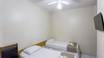 Ein Hotelzimmer mit zwei Einzelbetten, einem Deckenventilator, einem an der Wand montierten Fernseher und einem hölzernen Kopfteil.