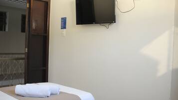 Habitación de hotel con dos camas, un televisor fijado a la pared y una puerta que da a otra habitación.