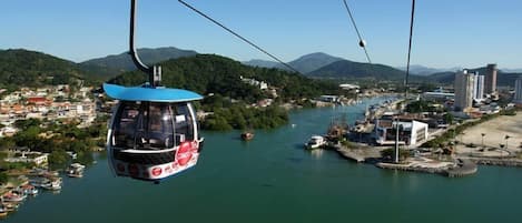 A cable car over a river with buildings and hills in the background.
