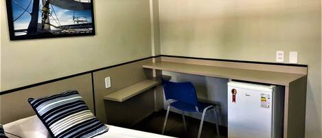 Habitación de hotel con cama, escritorio, silla y aire acondicionado instalado en la pared.