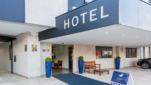 En hotelindgang med et skilt der viser ”HOTEL” og nummeret ”1473”. To træbænke står udenfor, og en blå måtte fører hen til indgangen.