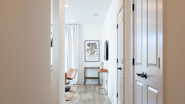 A hallway with a wooden floor, white walls, and a door on the right.