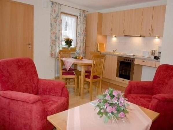 A compact living space with two red armchairs, a dining table with chairs, a kitchen area with wooden cabinets, and a small fireplace.