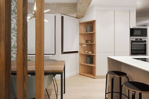 A modern kitchen with a wooden dining table, bar stools, and built-in shelves. - Hygge by FeelFree Rentals (Donostia)
