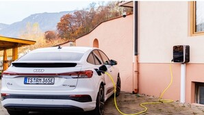Un coche blanco aparcado en una entrada con una estación de carga conectada a un edificio.