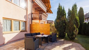 Un patio con mobiliario de mimbre y una mesa, una terraza de madera y un edificio con balcón.