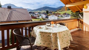 Een balkon met een tafel gedekt voor twee, met uitzicht op een dorp en bergen.
