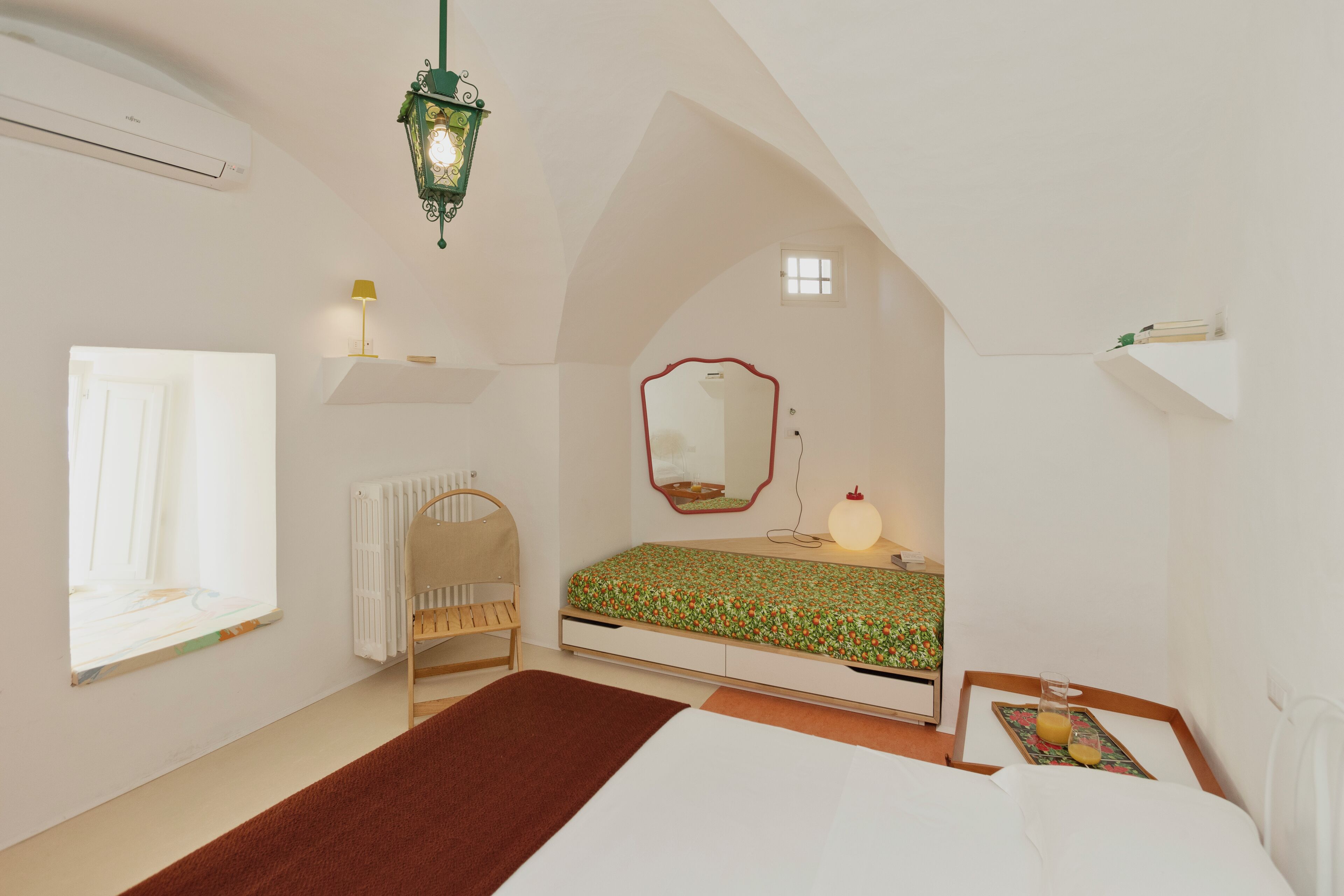 A bedroom with a sloped ceiling, a bed with a floral bedspread, a bedside table with a lamp, a window, and a radiator.