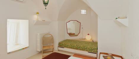 A bedroom with a sloped ceiling, a bed with a floral bedspread, a bedside table with a lamp, a window, and a radiator.