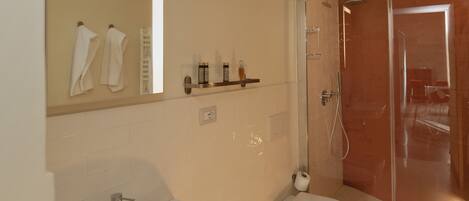A bathroom with a sink, toilet, and a glass-enclosed shower. There are towels hanging on the wall and a shelf with toiletries.