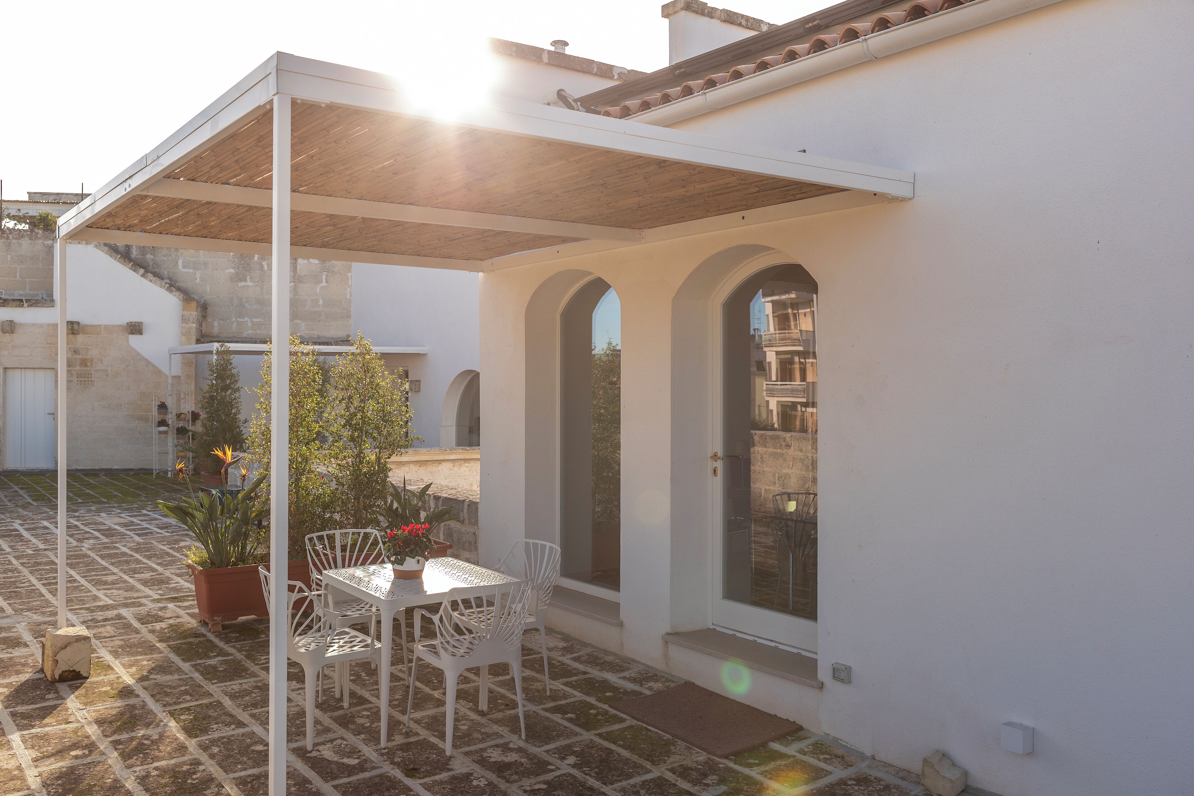 A covered patio area with a table and chairs, a potted plant, and a view of the surrounding buildings.