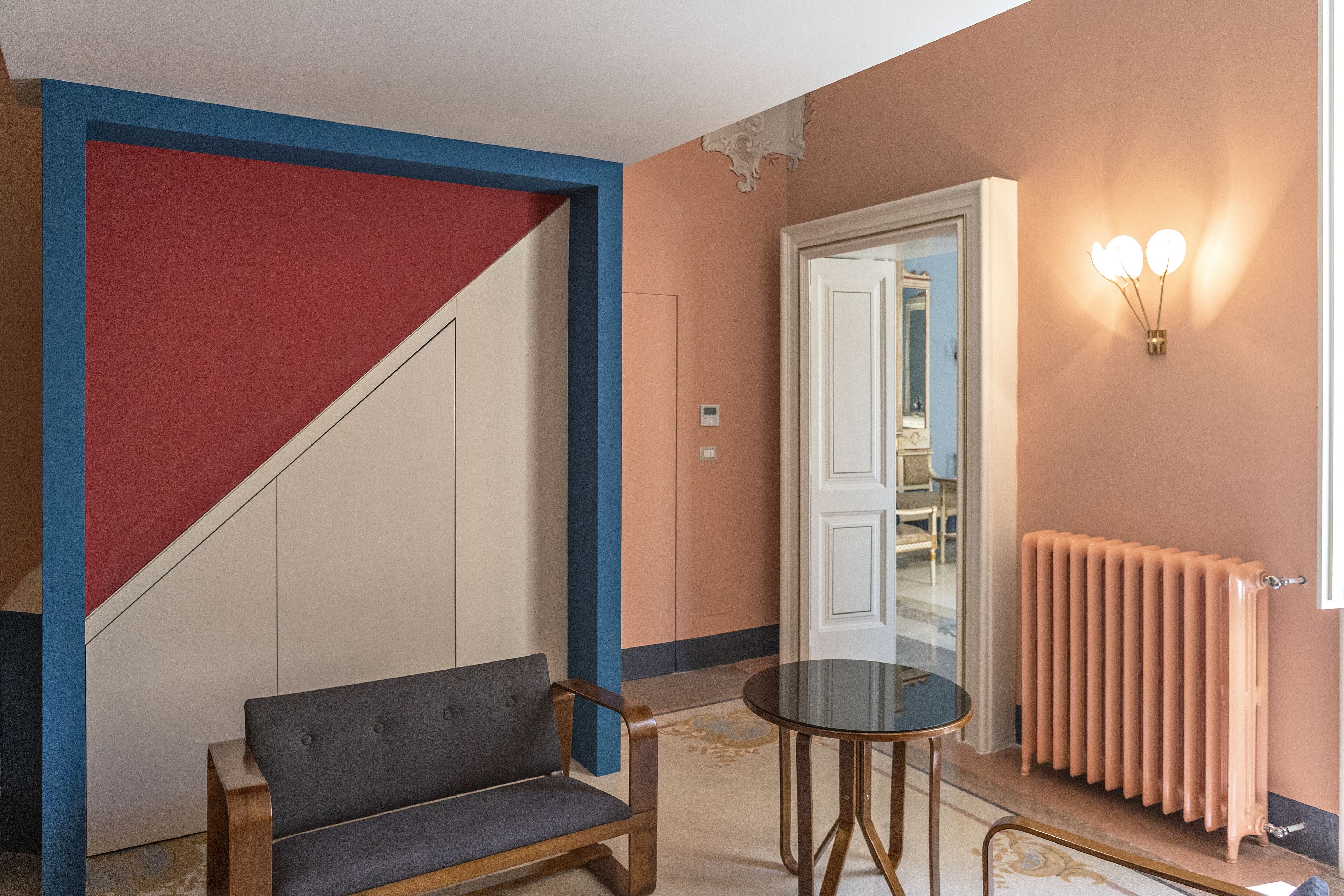 A hotel room with a sofa, a small round table, a radiator, and a door leading to another room.