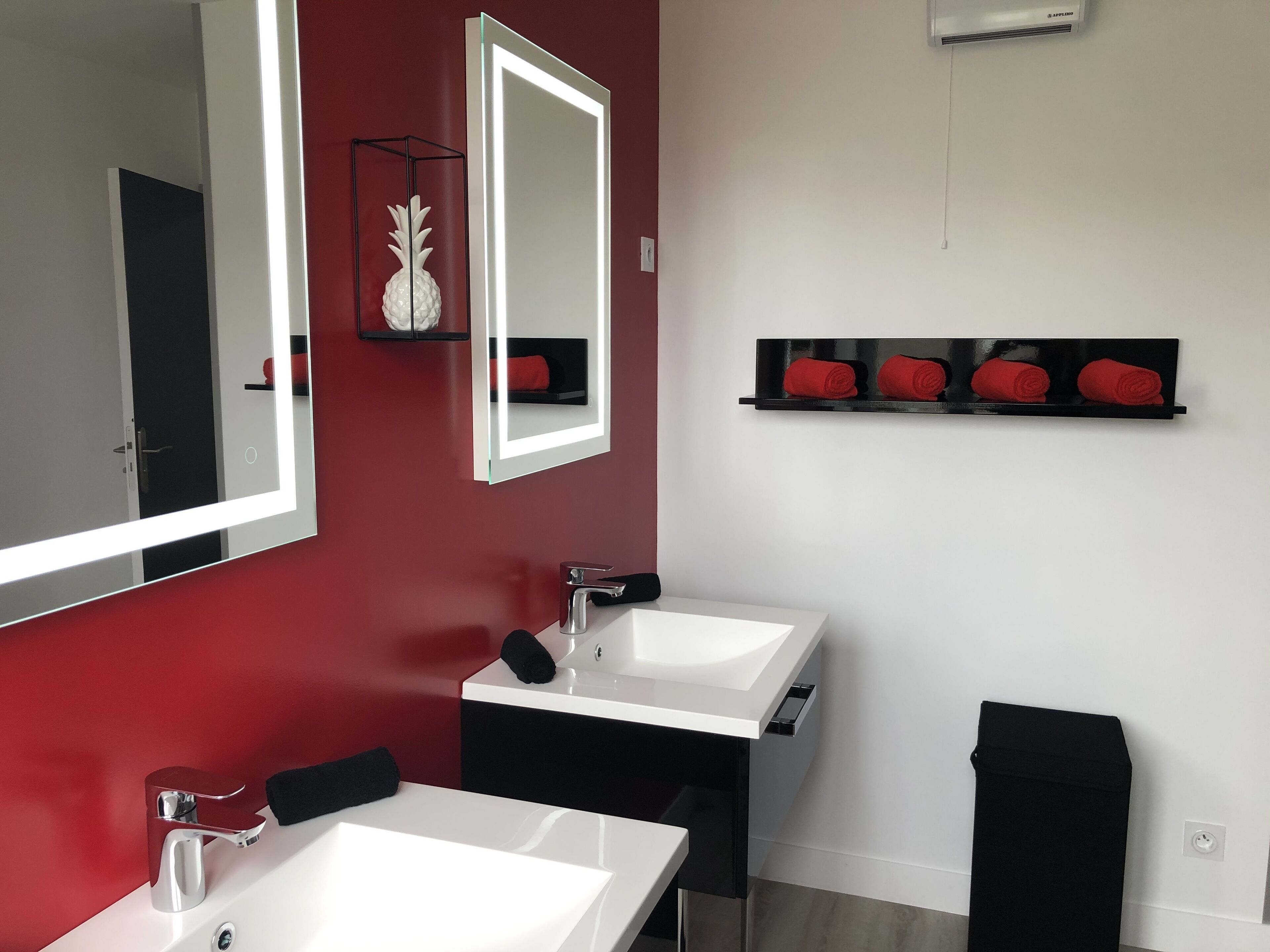 Een moderne badkamer met twee witte wastafels, een grote spiegel, een rode wand en een zwarte handdoekhouder.