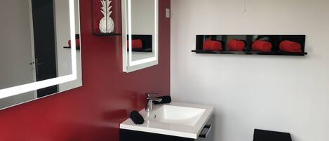 Een moderne badkamer met twee witte wastafels, een grote spiegel, een rode wand en een zwarte handdoekhouder.