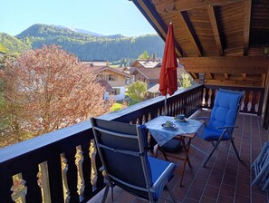 Uma varanda com mesa, cadeiras e um guarda-sol vermelho.
