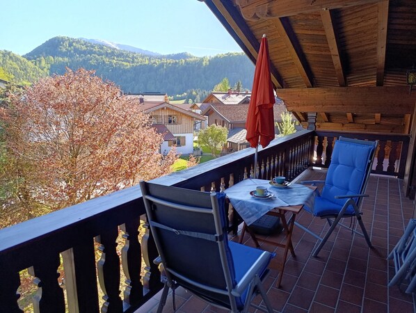 A balcony with a table, chairs, and a red umbrella.