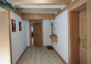 Un pasillo con vigas de madera, una puerta y un pequeño estante de madera con un gancho.