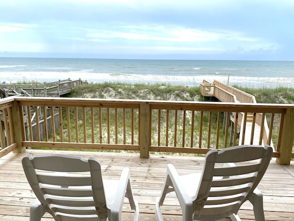 A wooden deck with two white plastic chairs facing a beach with wooden walkways and a boardwalk. - The Surf - Surf's Up! Oceanfront Getaway!! (North Topsail)