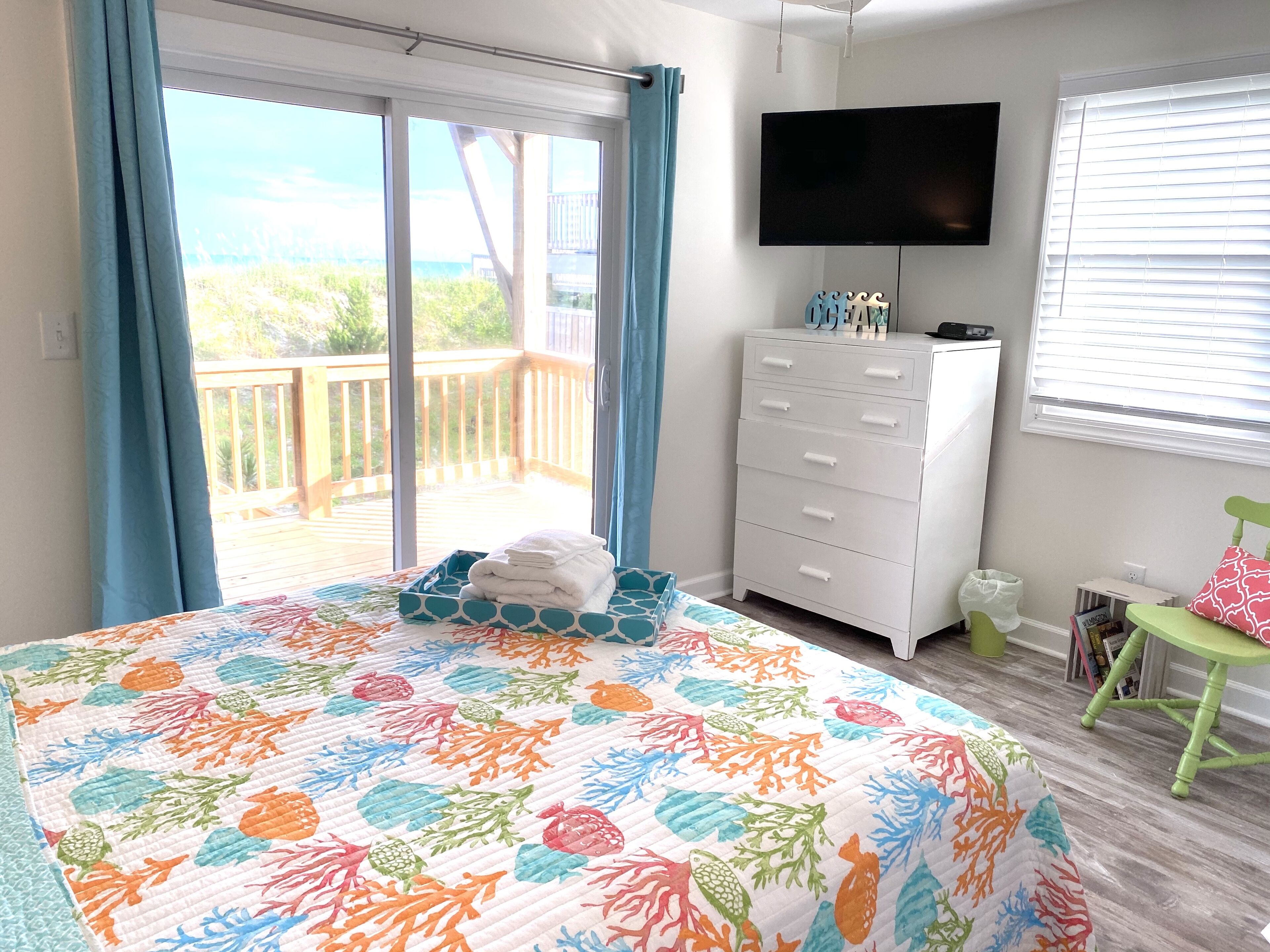 A bedroom with a bed, a dresser, a TV, and a view of the outdoors.