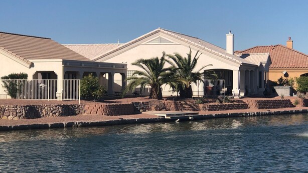 A waterfront property with a pool, a covered patio, and a stone retaining wall.