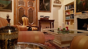 Un soggiorno tradizionale con divano, poltrona e tavolino da caffè con candele. Si nota una libreria e un caminetto sullo sfondo.