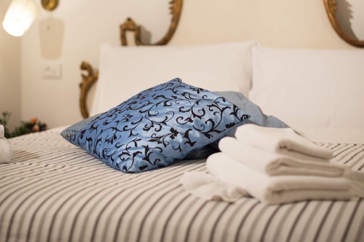 Cama bem arrumada com travesseiro azul estampado, travesseiros brancos e toalhas dobradas.