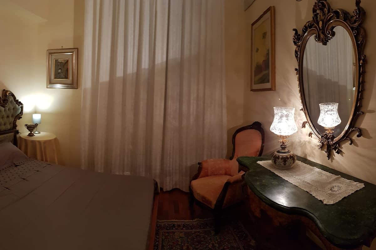 Quarto com uma cama grande, uma cadeira, uma mesa com abajur e um espelho.