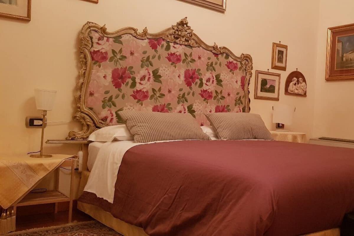 Quarto com cabeceira estampada, cama com colcha vermelha, mesa de cabeceira com abajur e criado-mudo.