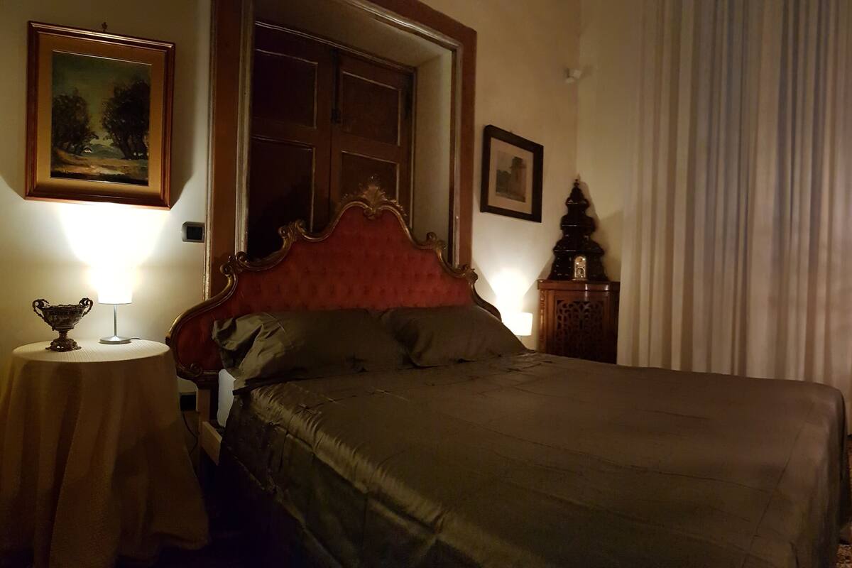 Quarto com cama, mesa de cabeceira, luminária, espelho e um quadro na parede.