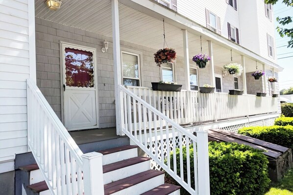 A white building with a covered porch, steps, and hanging flower baskets.