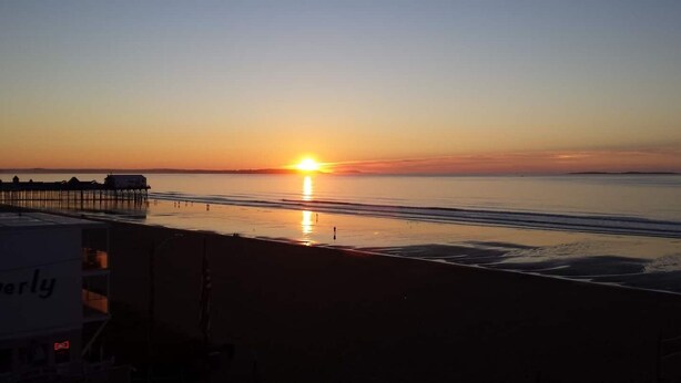 Una playa con un atardecer, un muelle y un edificio con la palabra 'erly'.