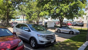 Un estacionamiento con coches, un sendero pavimentado y árboles.