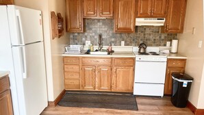 Una cocina con armarios de madera, un refrigerador blanco, una estufa y un cubo de basura.