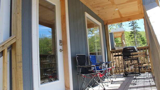 Una terraza de madera con zona cubierta, una parrilla y sillas plegables.