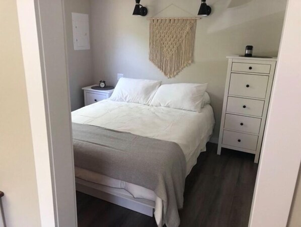 Un dormitorio con cama, mesitas de noche, cómoda y un colgador de macramé en la pared.