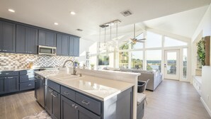 Une cuisine moderne avec des meubles de couleur sombre, un grand îlot central et une vue sur l’extérieur.