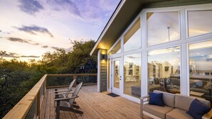 Une terrasse en bois avec des sièges extérieurs, de grandes fenêtres et une vue sur le paysage environnant.
