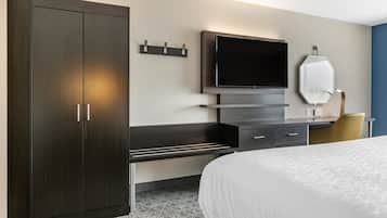 A modern hotel room with a large bed, a dark wooden wardrobe, a flat-screen TV mounted on the wall, a small desk with drawers, and a chair.