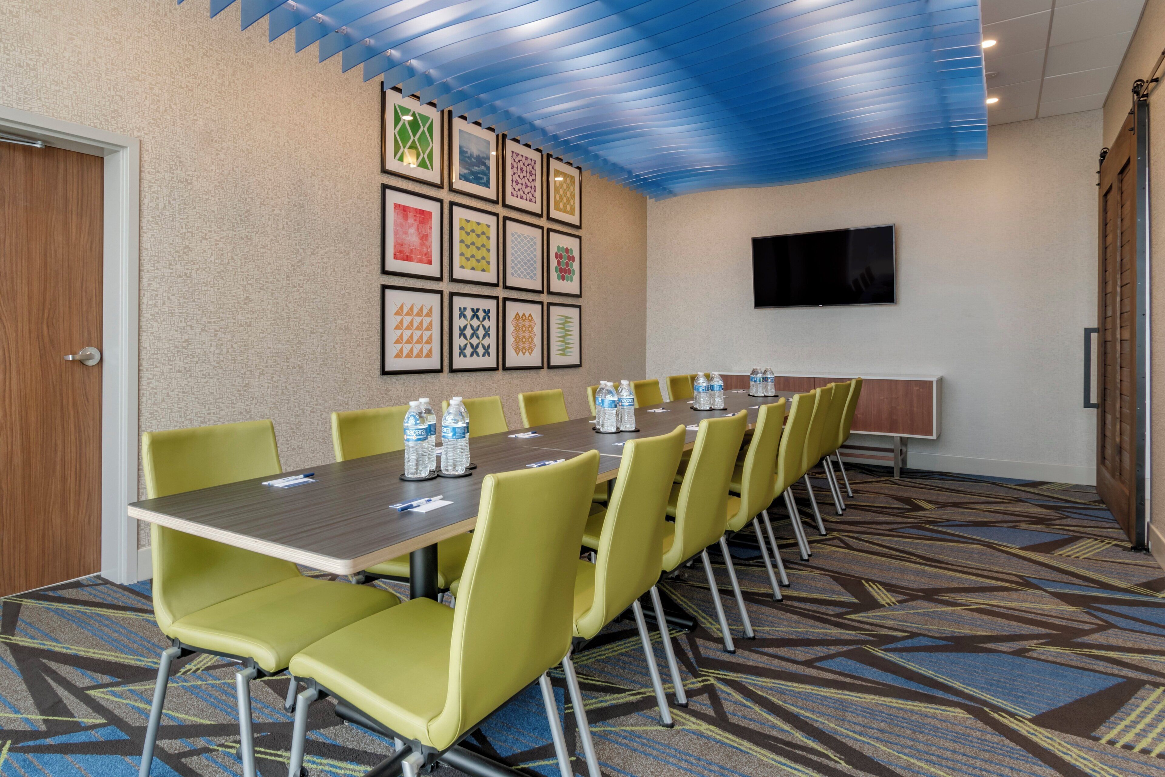 A conference room with a long table, yellow chairs, and framed artwork on the wall.
