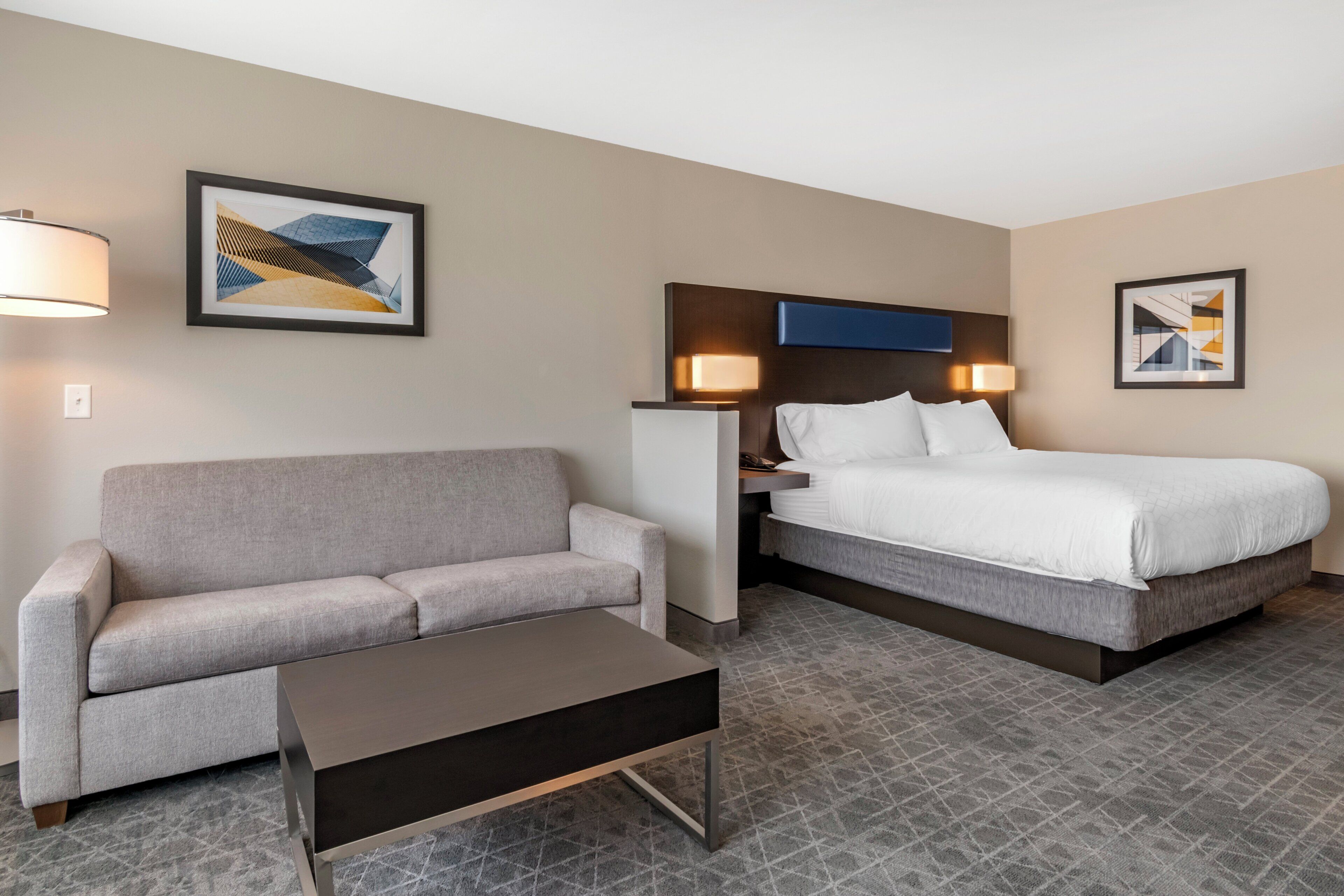 Ein Hotelzimmer mit einem grauen Sofa, einem Einzelbett, einem kleinen Tisch und zwei Wandlampen.