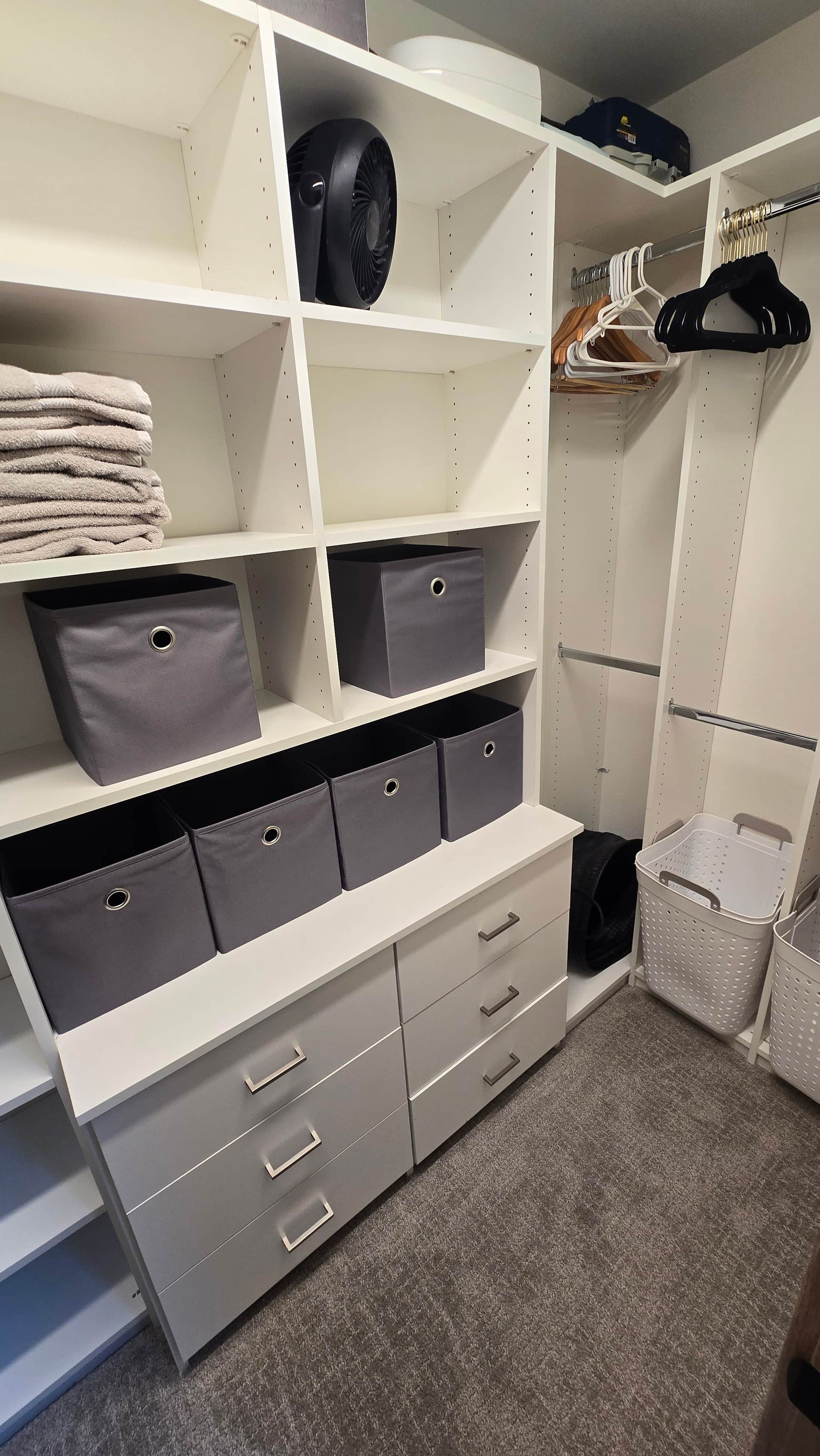 Een kast met planken, lades en een hanggedeelte, gevuld met opgevouwen kleding, opbergbakken en een ventilator.