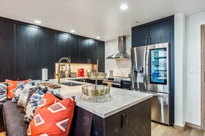 A modern kitchen with dark cabinets, stainless steel appliances, and a marble countertop. - Snowloft Ski In & Ski out (Beaver Creek)