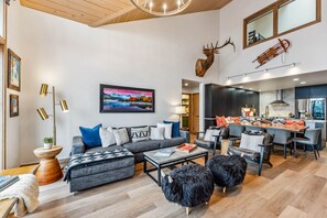 A modern living room with a sofa, coffee table, and decorative items. There is a kitchen area with a dining table and chairs. - Snowloft Ski In & Ski out (Beaver Creek)
