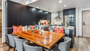A modern kitchen with dark cabinetry, a wooden dining table, and a built-in stove. - Snowloft Ski In & Ski out (Beaver Creek)