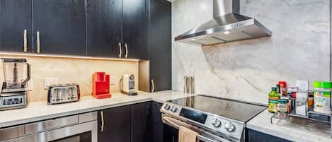Una cocina moderna con armarios oscuros, una estufa de acero inoxidable, horno empotrado, cafetera y cocina a gas.