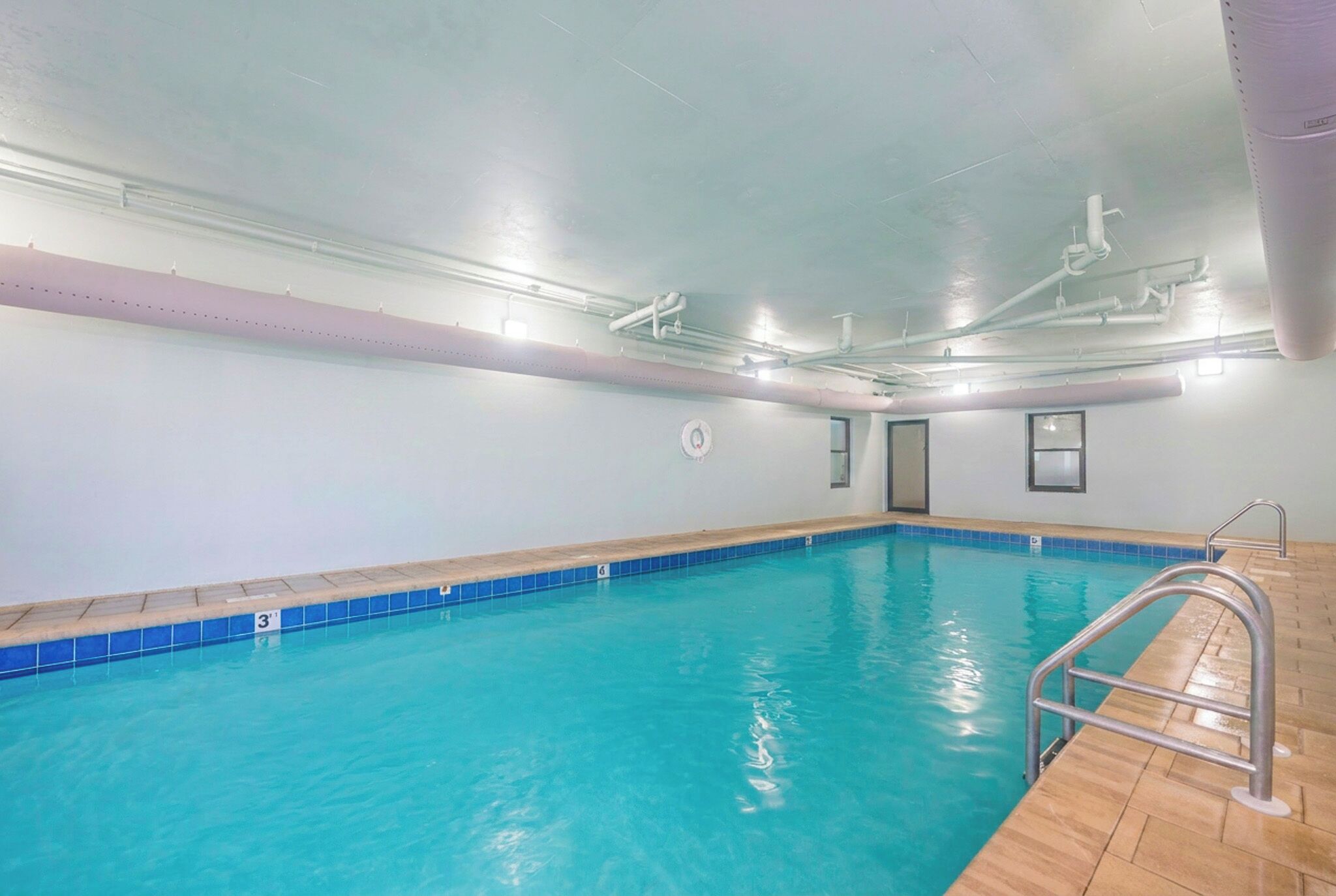 An indoor swimming pool with clear water, a tiled edge, and a metal ladder on the right.