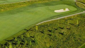 Golfkenttä, jossa on hiekkabunkkereita, majakka ja metsäinen alue.