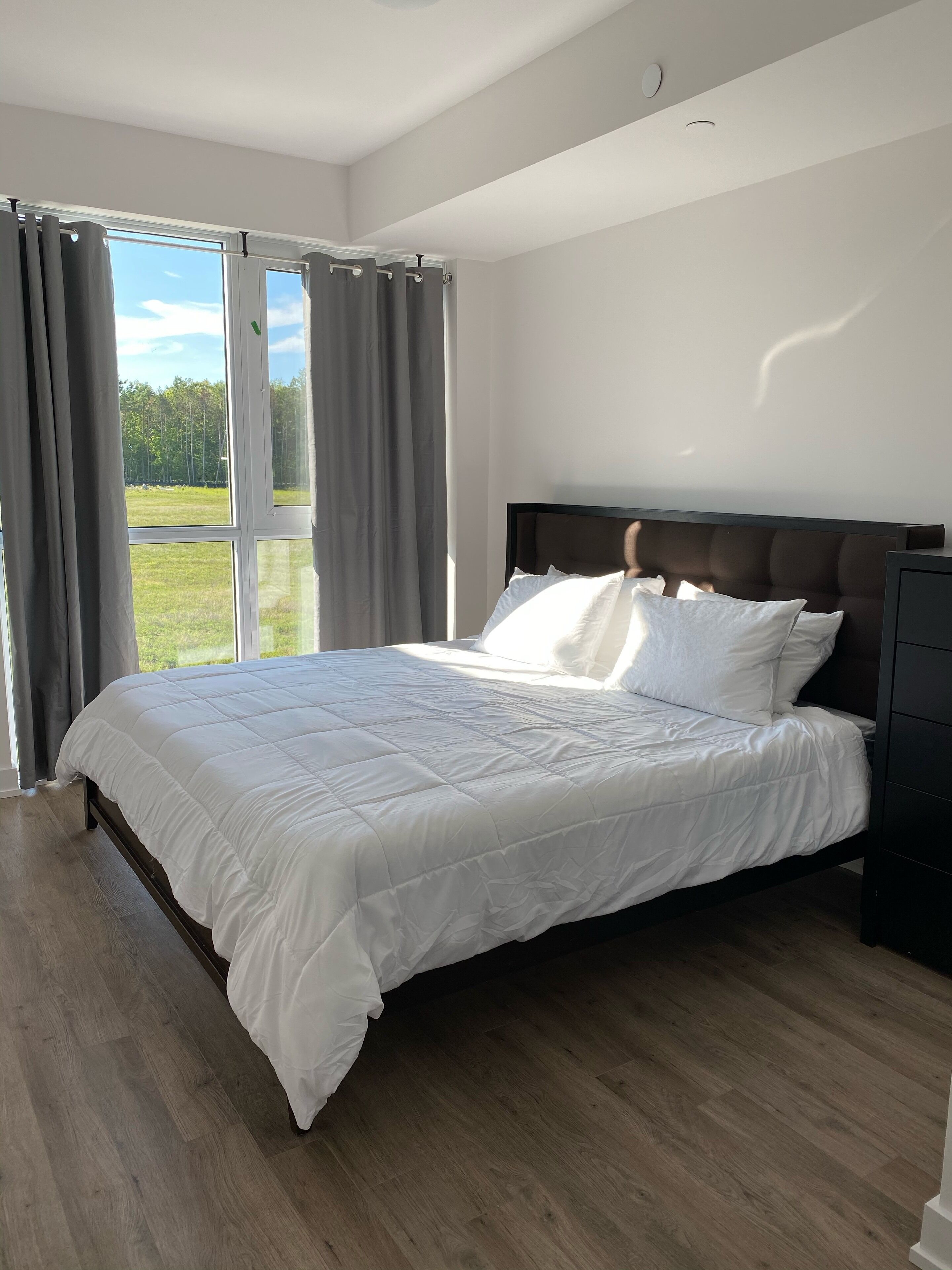 A bedroom with a large bed, a wooden floor, and a view of a grassy field through the window.