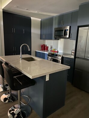 A modern kitchen with dark cabinets, stainless steel appliances, a marble countertop, and bar stools. - Friday Harbour Resort on Lake Simcoe (Innisfil)