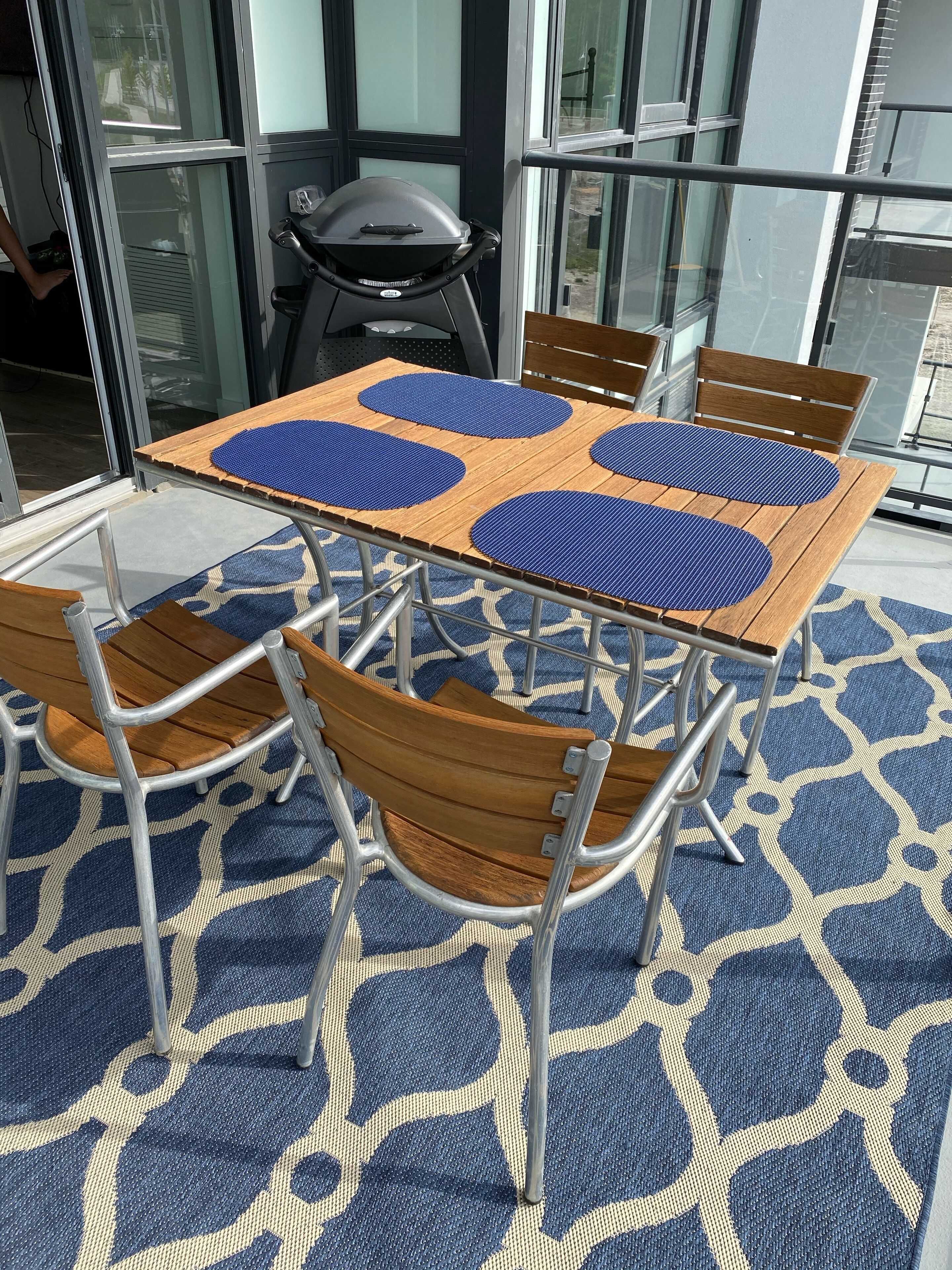 A table with four blue mats, surrounded by six wooden chairs with metal frames, set on a patterned floor.